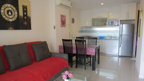 A living room with a red sofa, a dining area with a table and chairs, a kitchen with a refrigerator and microwave, and a ceiling fan. - SUPER 404 LUXURY APARTMENT, QUIET, IN THE DINAMIQUE DISTRICT OF JOMTIEN. (Jomtien)