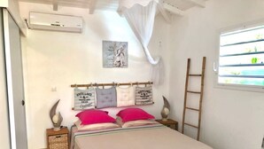 Une chambre à coucher comprenant un lit, des tables de chevet, une fenêtre avec des stores, une échelle et un climatiseur fixé au mur.