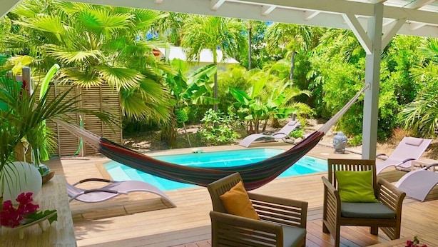 Un espace aménagé au bord de la piscine, avec un hamac, des chaises longues et une terrasse en bois.