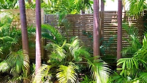 Un jardin luxuriant, avec de grands palmiers et un feuillage dense, entouré d’une clôture en bois.