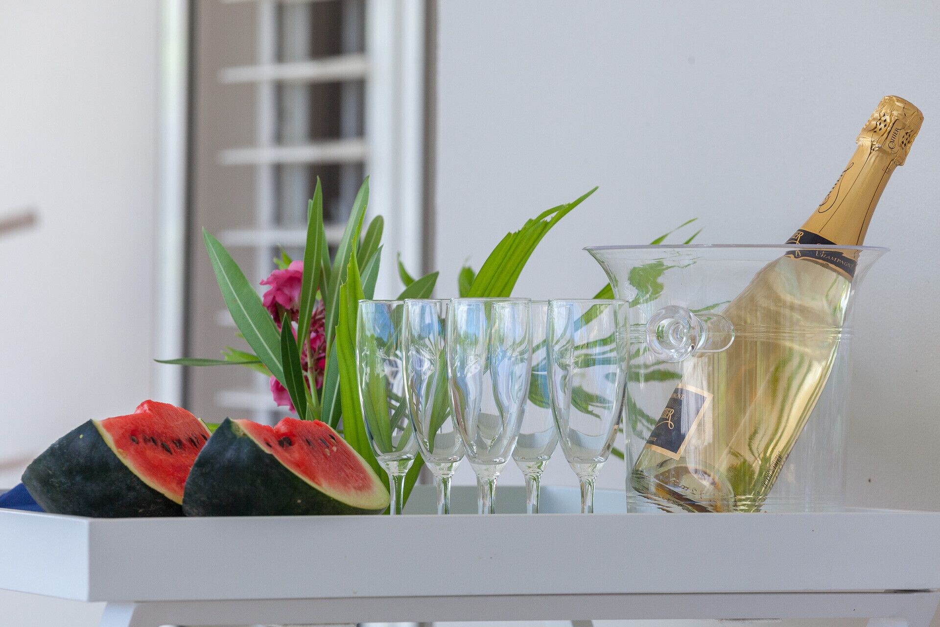 A white table with a champagne bottle, glasses, and watermelon slices.