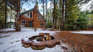 A log cabin with a fire pit in a snowy forest.