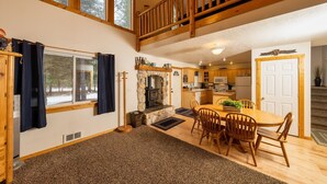 A cozy cabin interior with a stone fireplace, wooden dining table, and a loft bedroom with a wooden railing.