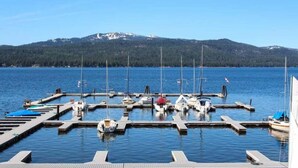 A marina with boats docked, surrounded by a calm lake and a forested mountain range in the background.