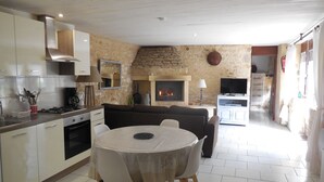 Eine moderne Küche mit weißen Schränken, einem Esstisch mit Stühlen, einem Kamin aus Stein und einem Fernseher im Wohnbereich.