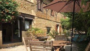 Ein rustikales Steinhaus mit einer Terrasse, die Holzmöbel und einen Tisch bietet.