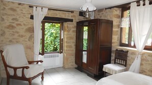 Ein Zimmer mit einer Steinsäule, einem Holzschrank, einem Stuhl, einem Bett und einem Fenster mit Vorhängen.