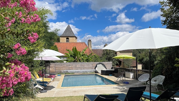 Ein Garten mit Schwimmbad, Liegestühlen, Sonnenschirmen und einem kleinen Tisch.