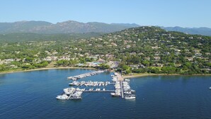A marina with numerous boats docked, surrounded by a residential area with houses and greenery, and mountains in the background.