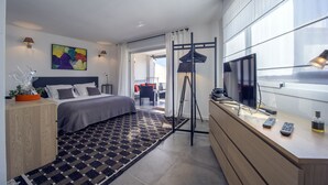 A modern hotel room with a bed, bedside table, TV, and a view of the outside.