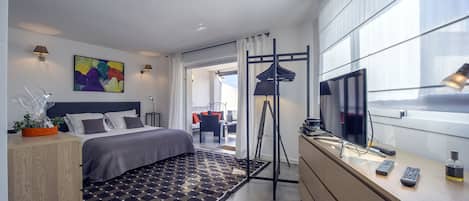 A modern hotel room with a bed, bedside table, TV, and a view of the outside.