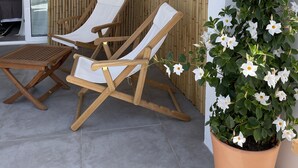 A patio with two wooden lounge chairs, a small table, and a potted plant with white flowers.
