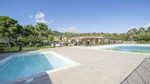 A swimming pool area with a tiled deck, a pergola structure, and a view of a hillside with buildings.