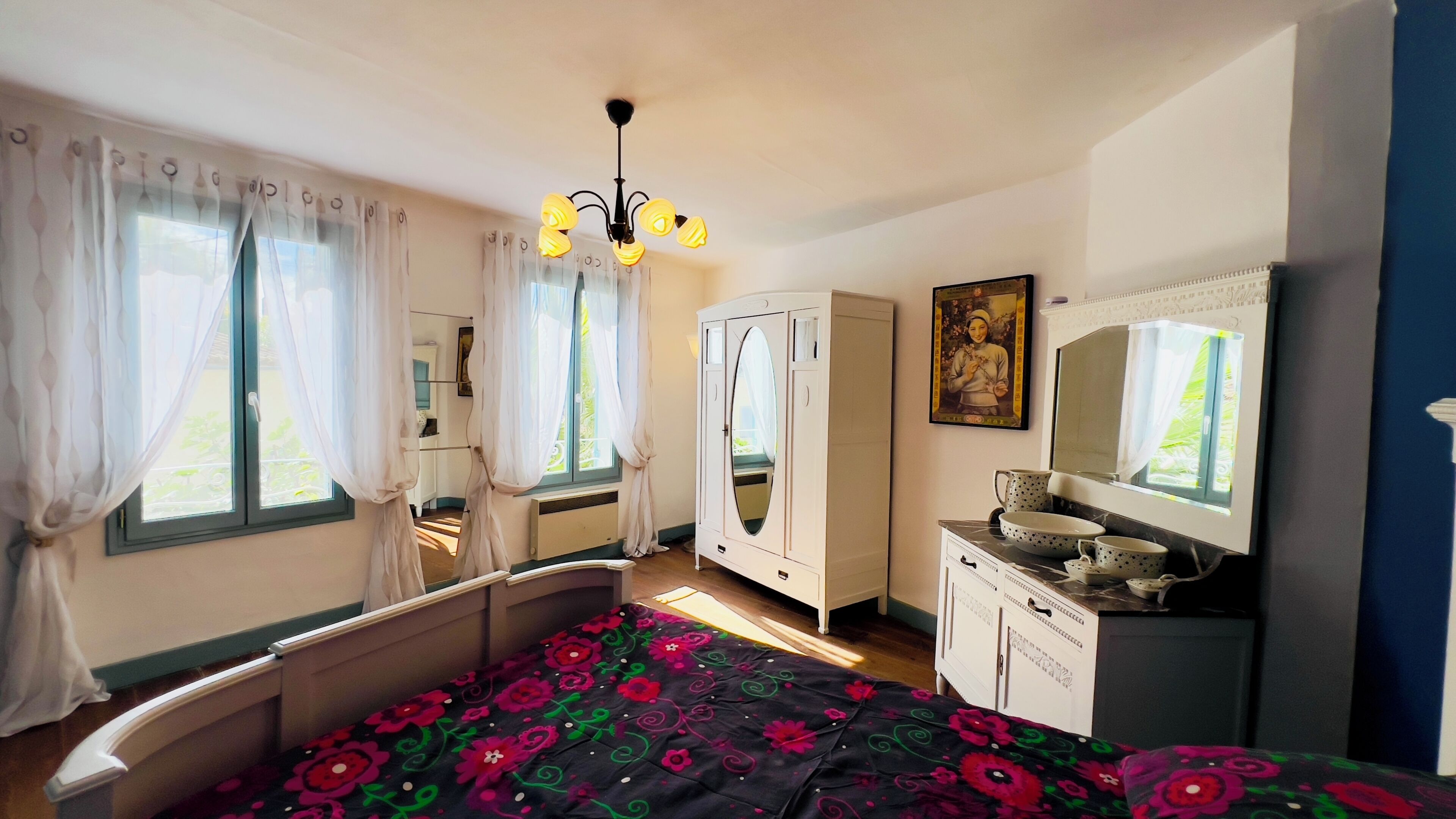 A bedroom with a bed, a wardrobe, a vanity with a mirror, and a chandelier.