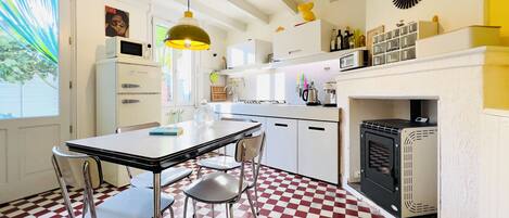 Une cuisine avec un carrelage à motifs, des placards blancs, une table à manger avec des chaises, un four à micro-ondes, une machine à café et une cuisinière.