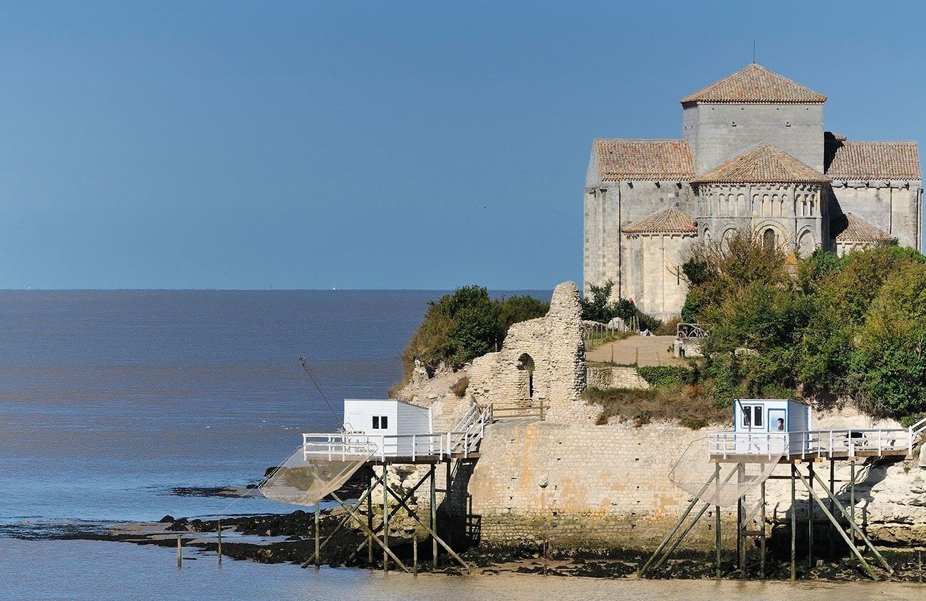 A historic stone building with a tower, situated on a cliff overlooking the sea.