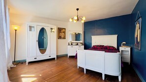 Un dormitorio con cama, armario, cómoda, espejo, candelabro y pared azul.