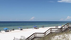 A beach with white sand, clear blue water, and a wooden staircase leading down to the beach. There are blue umbrellas and beach chairs set up for sunbathing. - THE PEARL at the Emerald Coast 1 Duplex (Santa Rosa Beach)