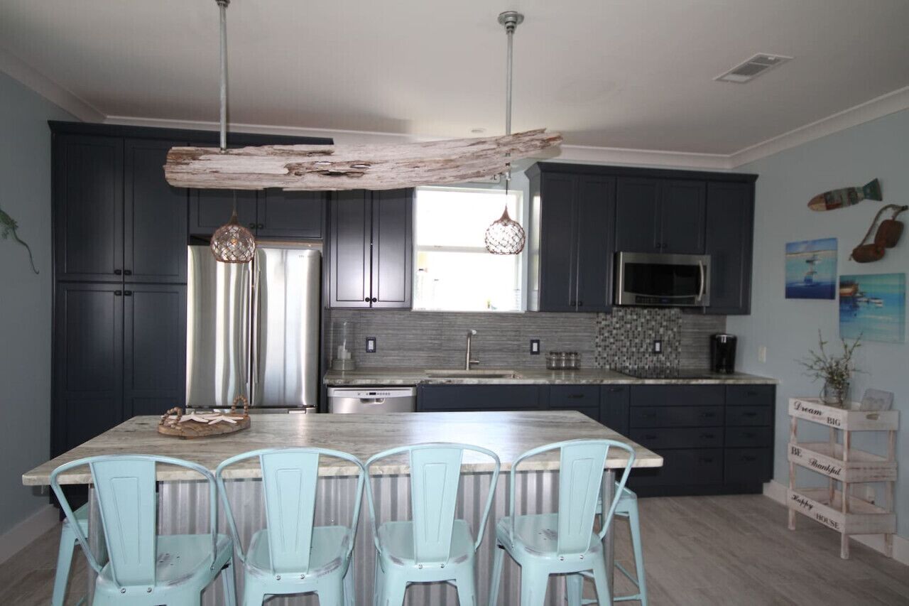 Une cuisine moderne avec des meubles de couleur sombre, un grand îlot central doté de chaises, un luminaire suspendu et une poutre rustique au plafond.