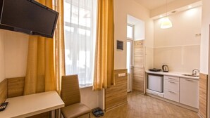 A compact hotel room with a kitchenette, a seating area with a table and chair, and a TV mounted on the wall.