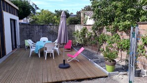 A wooden deck with a table and chairs, a red lounge chair, and a potted plant.