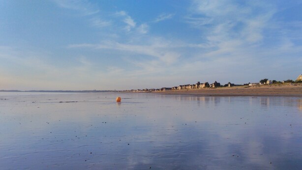 A wide, flat beach with a clear sky and a few buildings in the distance.