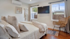 Ein Schlafzimmer mit Bett, Sessel, Fernseher und einem Fenster mit Vorhängen.
