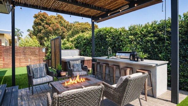 Eine Terrasse im Freien mit Feuerstelle, Korbmöbeln und einer Bar.