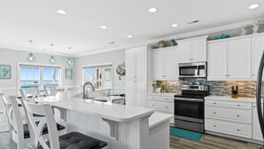 Una cocina moderna con armarios blancos, una isla central, electrodomésticos de acero inoxidable e iluminación colgante.
