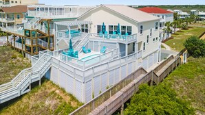 Una propiedad frente a la playa con varios pisos, piscina, asientos al aire libre y una terraza de madera.