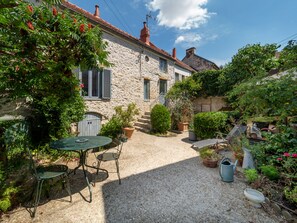 Una casa de piedra con un patio de grava, una mesa con sillas y diversas plantas en macetas.