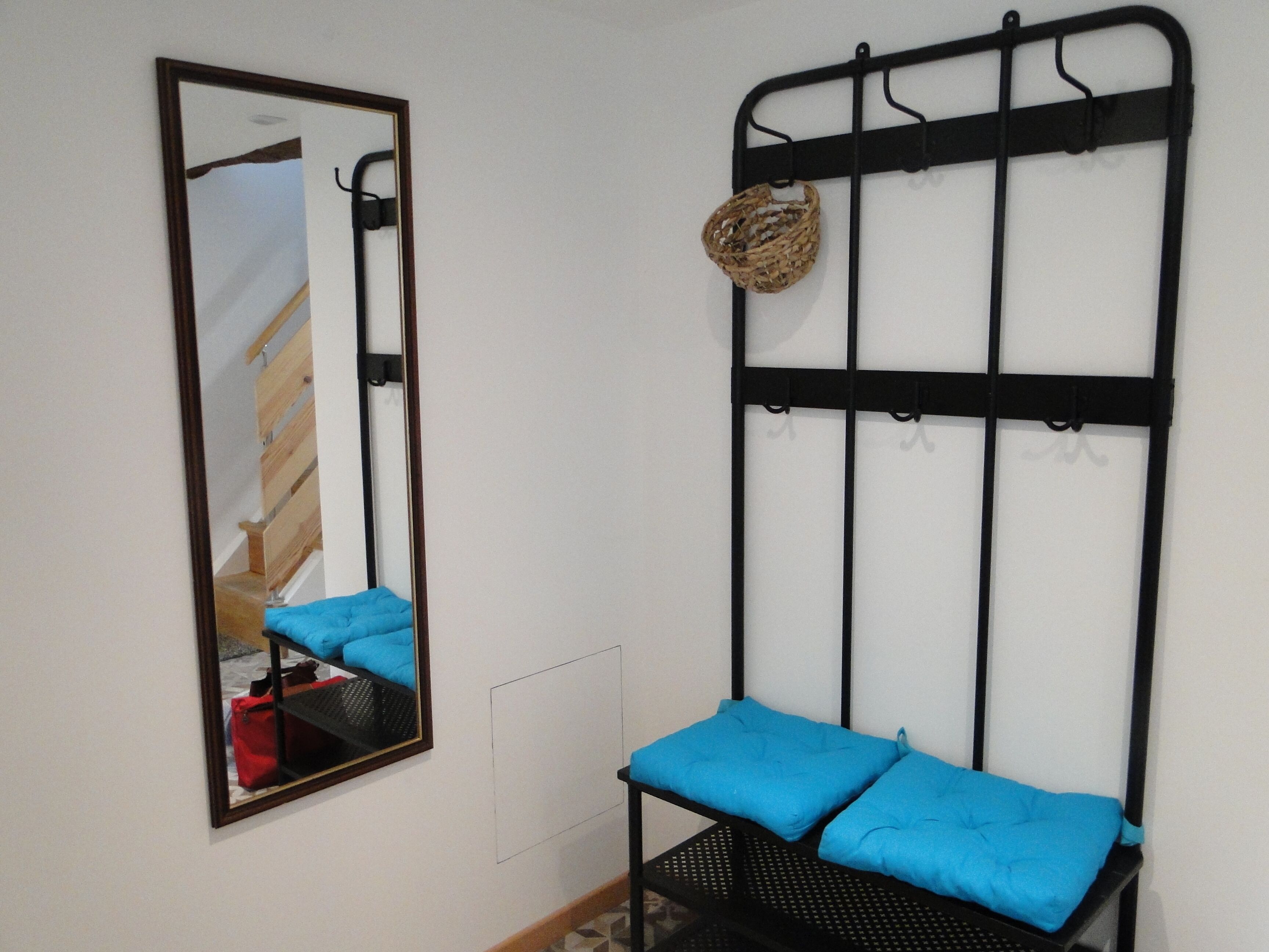 Une chambre avec une tête de lit en métal noir dotée de crochets, un miroir et un banc rembourré bleu.