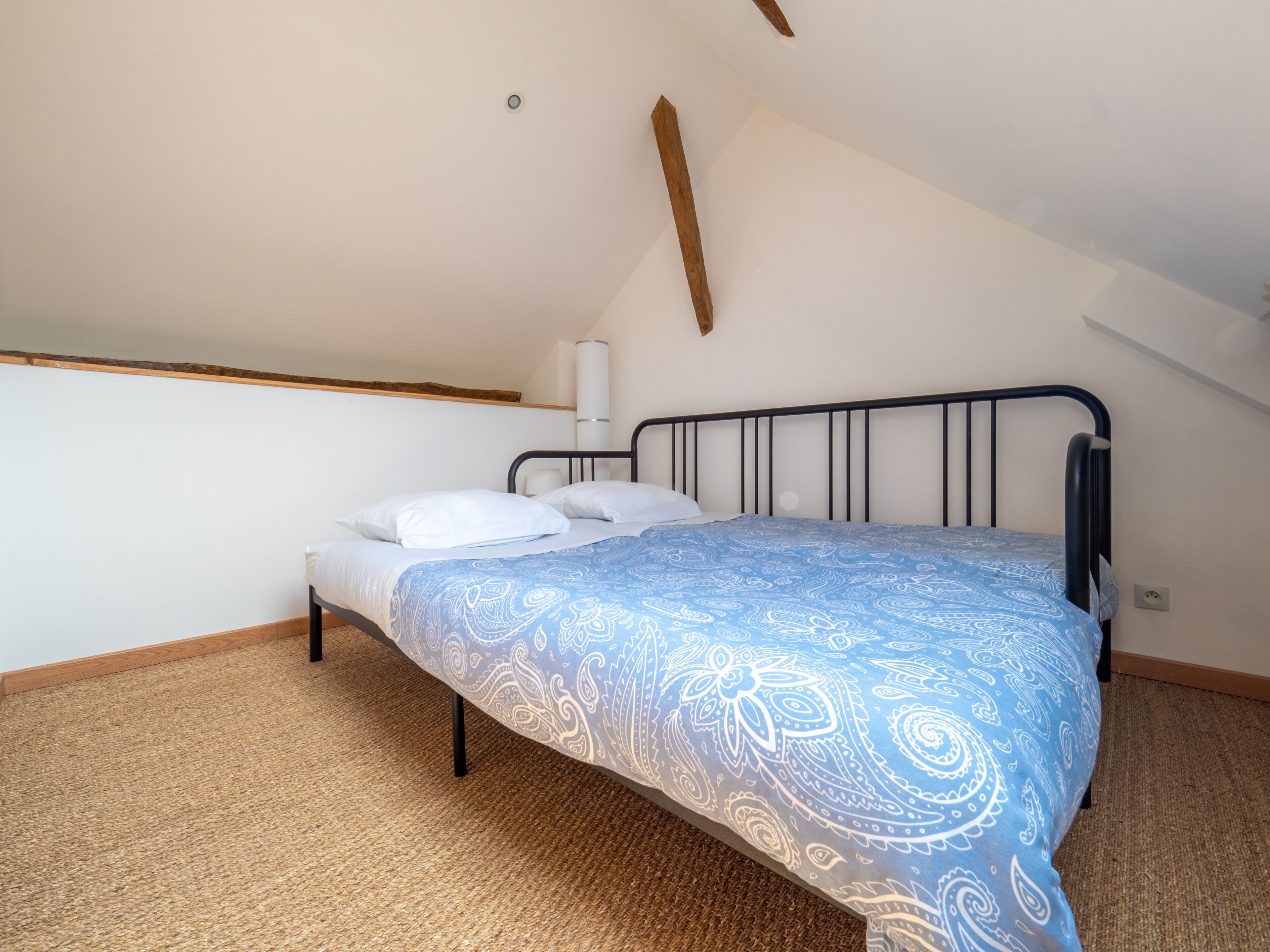 Un dormitorio con cama, lámpara de pared y techo inclinado.