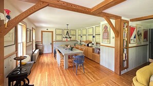 A spacious kitchen with wooden beams, a dining area with chairs, a coffee table, and a built-in bookshelf.