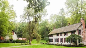 A large house with a prominent tree in front, surrounded by lush greenery.