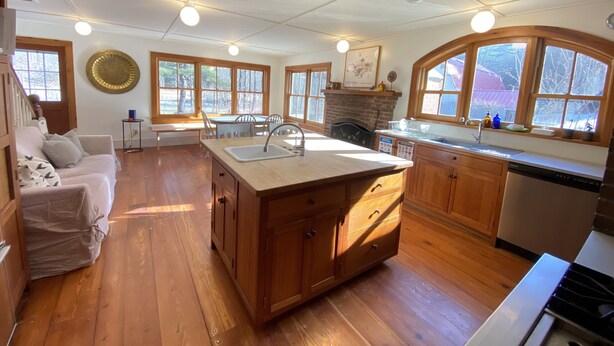 A spacious kitchen with wooden cabinets, a large island with a sink, and a stone fireplace.