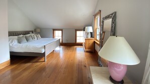 A bedroom with a bed, wooden flooring, a window, a lamp, and a mirror.