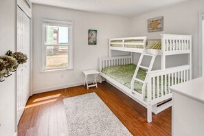 A child's room with bunk beds, a small table, a window with a view, and a wall decoration.