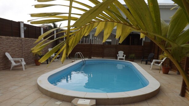 Et rektangulært swimmingpool med fliseterrasse, omgivet af krukker med planter og hvide plastikstole.