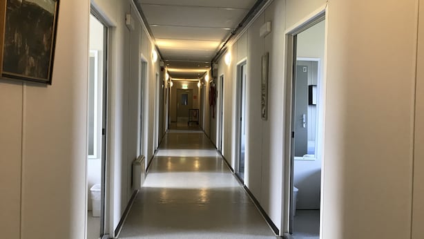 Een lange, smalle hotelgang met deuren aan beide kanten, een gepolijste vloer en verlichting in het plafond.