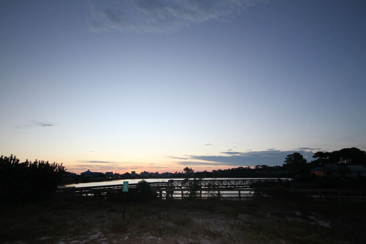 A sunset view over a bridge with a grassy foreground and distant buildings.