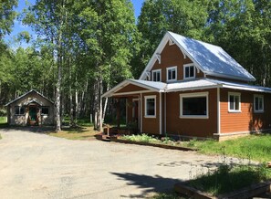 A two-story cabin with a porch, surrounded by a forest.