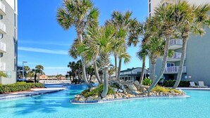 A swimming pool surrounded by palm trees and a building with balconies. - 3 Bedroom in Long Beach Resort ~ Beautiful with beach chairs included! (Panama City Beach)