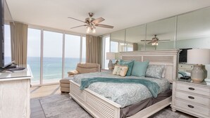 A bedroom with a large bed, a desk, and a chair. There are two ceiling fans and a large window with a view of the ocean. - 3 Bedroom in Long Beach Resort ~ Beautiful with beach chairs included! (Panama City Beach)