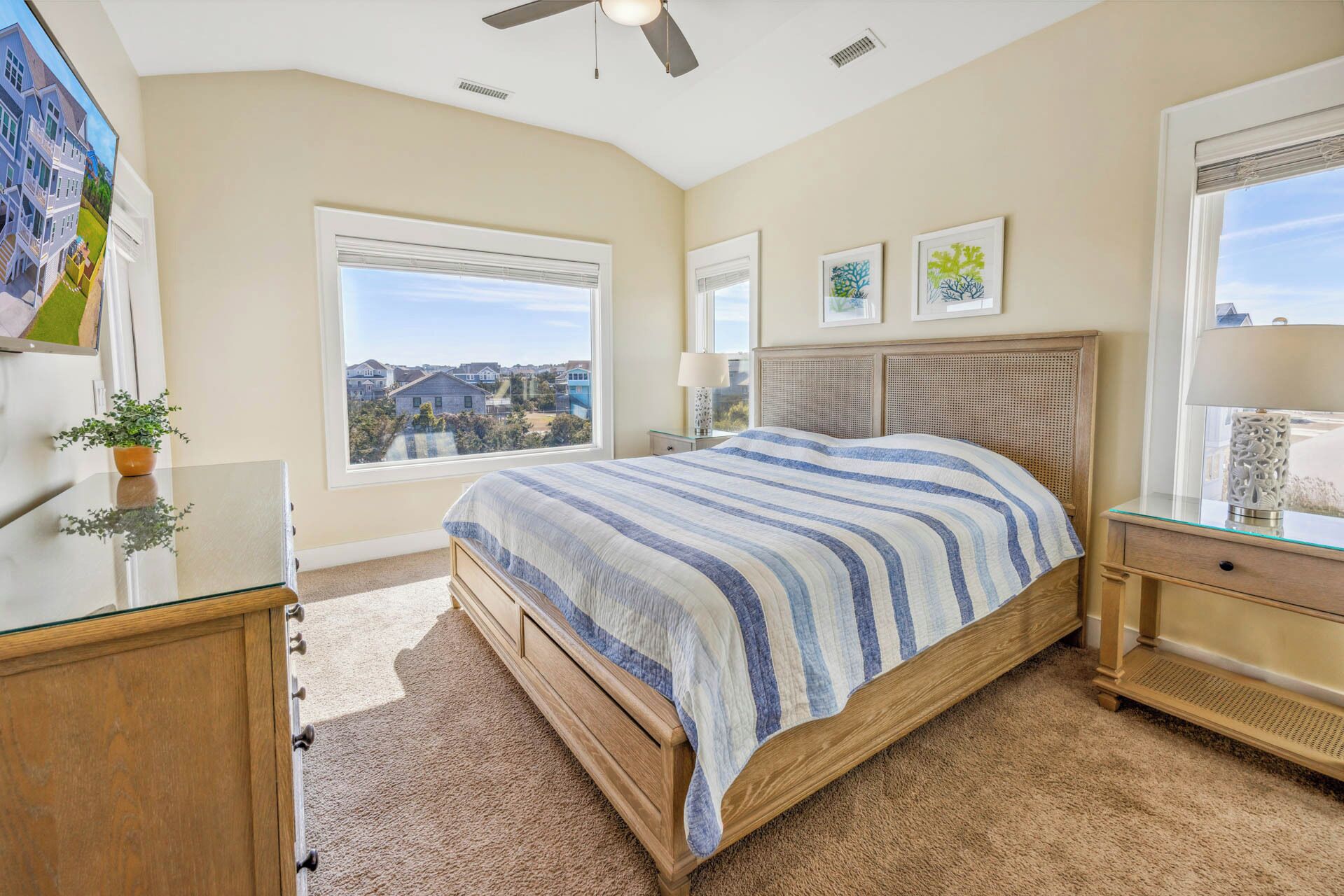 A bedroom with a large bed, a ceiling fan, a window with a view, and a bedside table with a lamp.