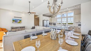 A spacious dining area with a wooden table set for six, a grey sofa, and a kitchen in the background.