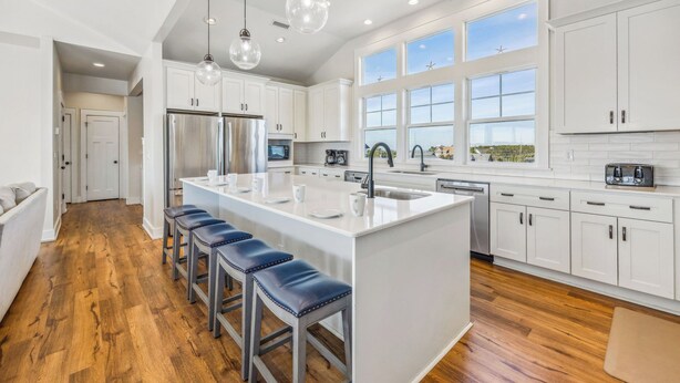 A modern kitchen with a large island, white cabinetry, and a wooden floor.