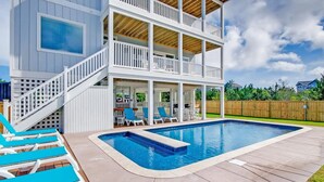 A two-story house with a pool, outdoor seating, and a wooden deck.