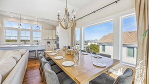 A spacious kitchen with a large dining table set for six, modern appliances, and large windows offering a view of the neighborhood.