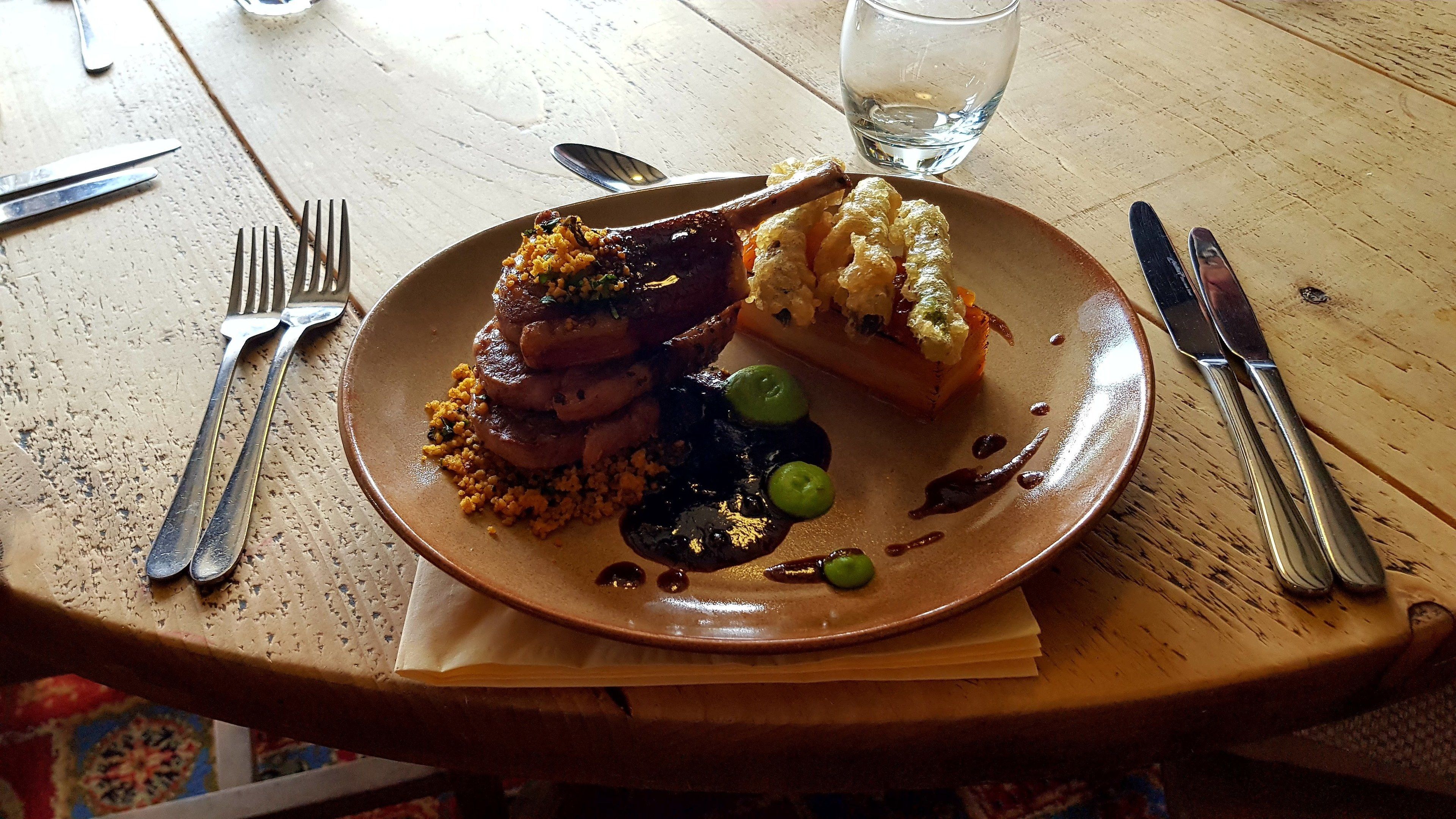 A plate of food on a wooden table with a fork, knife, and spoon to the left.
